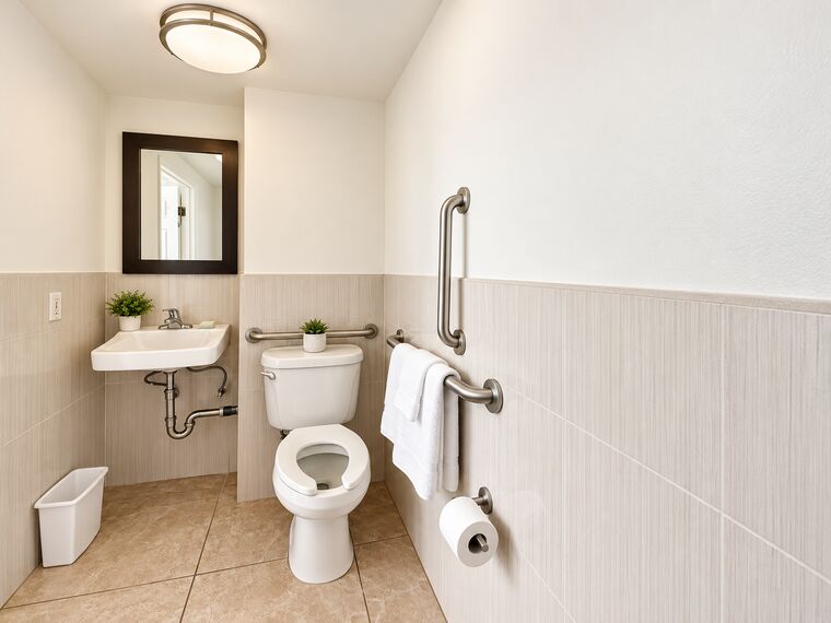 ADA bathroom with grab bars beside the toilet and on the wall, a wall-hung sink with clear space beneath and a framed mirror.