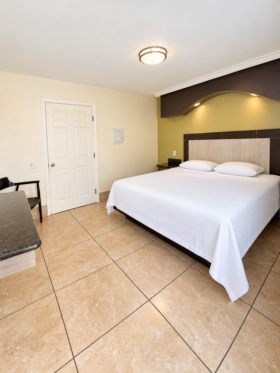 ADA room with a king bed in white bedding, tiled floor throughout and clear floor space beside the bed.