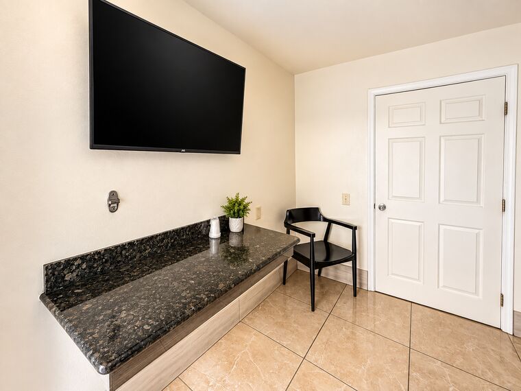 ADA room desk area with a granite counter, a wall-mounted television and a chair beside the door.
