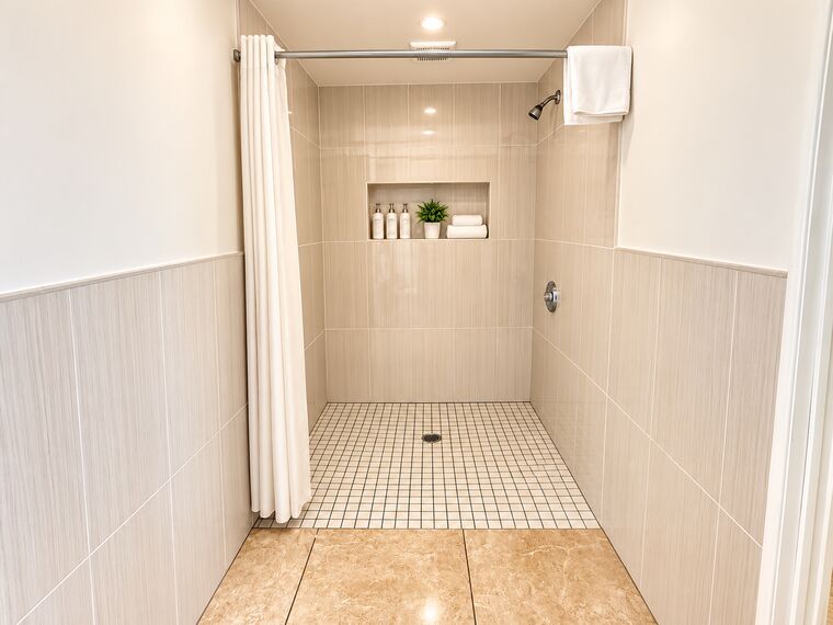 Roll-in shower in the ADA room: a step-free tiled shower with a curtain, a recessed shelf for toiletries and a towel on the rail.