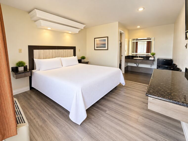 King Bed room with one king bed in white bedding, an open granite vanity beside the bathroom door and a framed print above the headboard.