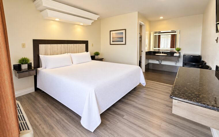 A King Bed room with one king bed in white bedding and an open granite vanity beside the bathroom door.