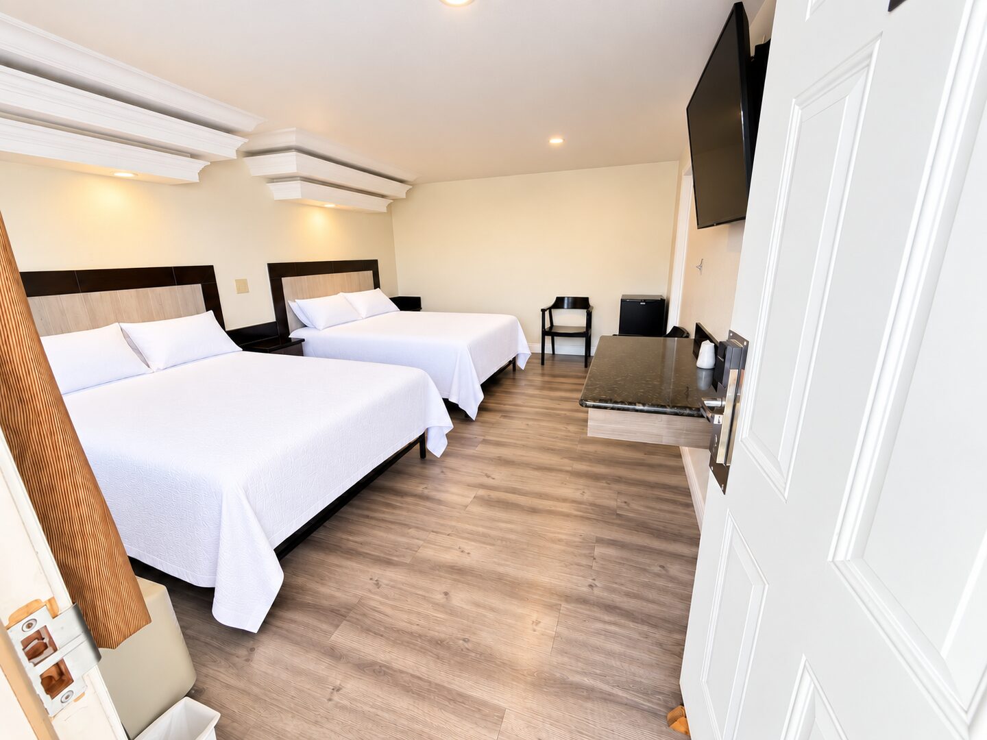 Two queen beds made up in white bedding, with a wall-mounted flat screen, a granite counter and a mini fridge along the opposite wall.