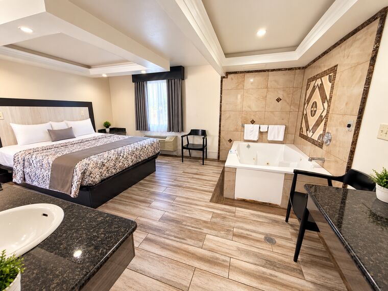 King Suite Spa seen from the vanity, with the king bed on the left and a jetted spa tub set into a tiled surround on the right.