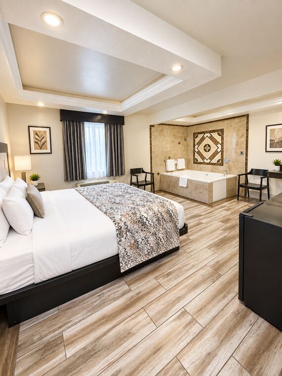King Suite Spa looking across the king bed to the jetted spa tub beneath a tiled medallion, with a desk and mini fridge to one side.